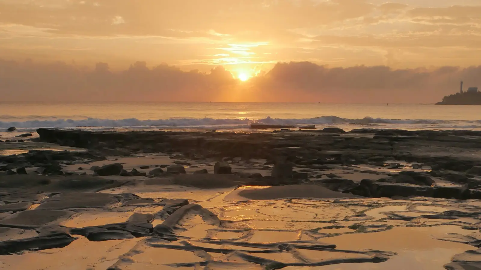 A rock platform on the shore at sunrise, with tide pools and gentle surf